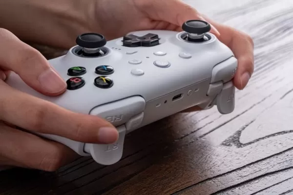 Una foto di una persona che tiene un controller di gioco bianco su una scrivania di legno
